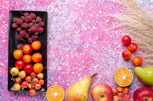 Vista dall'alto di lamponi e prugne di frutta fresca all'interno della forma nera sulla superficie rosa