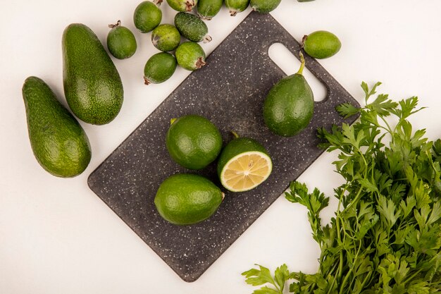 Vista dall'alto di limette di agrumi verdi su una tavola da cucina con avocado feijoas e prezzemolo isolato su un muro bianco
