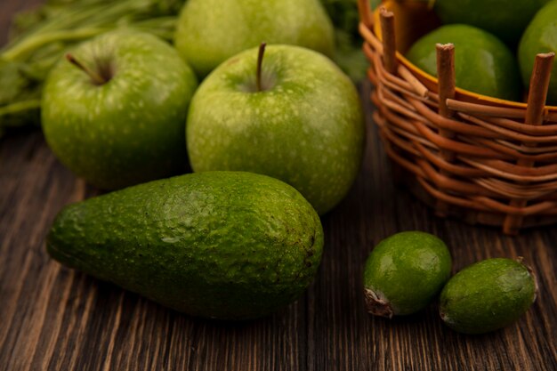 Vista dall'alto di limette fresche su un secchio con mele verdi avocado feijoas isolato su una parete in legno