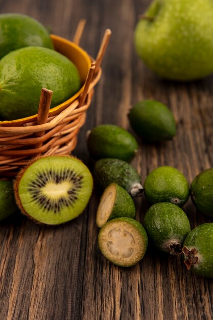 Vista dall'alto di limette mature su un secchio con mele verdi kiwi feijoas isolato su una parete in legno