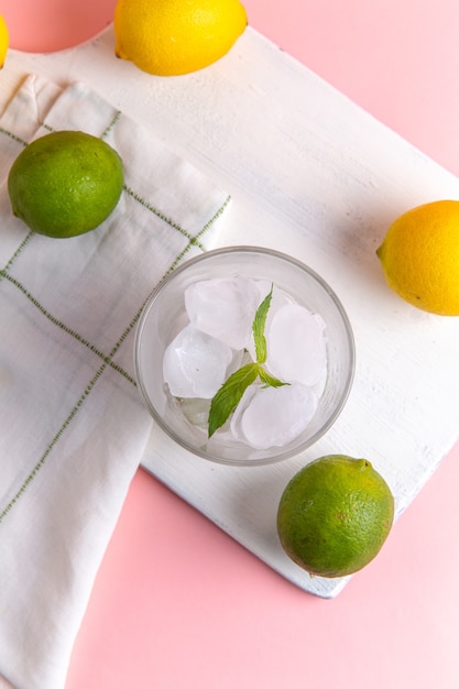 Vista dall'alto di limonata fresca fredda con ghiaccio insieme a limoni freschi sulla superficie rosa