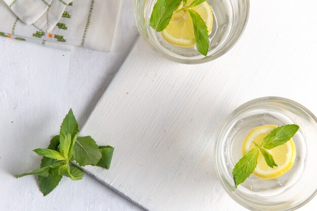 Vista dall'alto di limonata fresca fresca con limoni a fette all'interno di bicchieri su superficie bianco chiaro