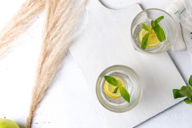 Vista dall'alto di limonata fresca fresca con limoni a fette all'interno di bicchieri sulla superficie bianca