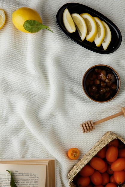 Vista dall'alto di limone e marmellata con mestolo di marmellata e kumquat con libro aperto su sfondo di stoffa bianca