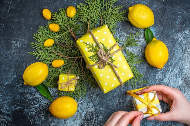 Vista dall'alto di limoni freschi con foglie di kumquat su rami di abete mano che tiene una confezione regalo su sfondo scuro