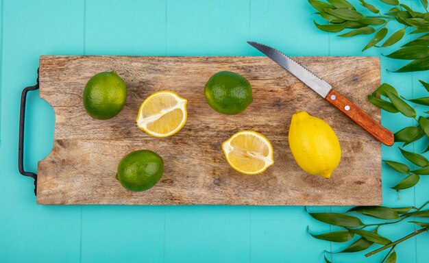 Vista dall'alto di limoni freschi e colorati sulla tavola di cucina in legno con coltello con foglie sul blu