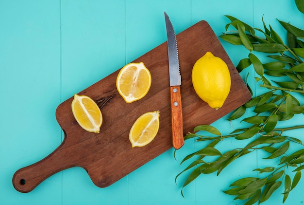 Vista dall'alto di limoni freschi e gialli sul bordo della cucina in legno con coltello con foglie sul blu