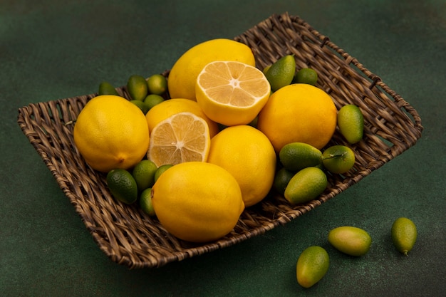 Vista dall'alto di limoni gialli su un vassoio di vimini con kinkan isolato su una parete verde