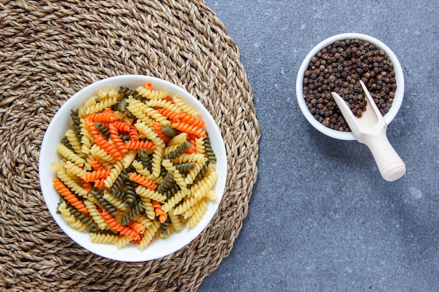 Vista dall'alto di maccheroni colorati pasta in una ciotola con pepe nero su sottopentola e superficie grigia. orizzontale