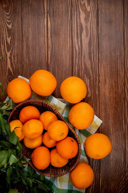 vista dall'alto di mandarini freschi in un cesto di vimini e arance mature sul tavolo di legno rustico con spazio di copia
