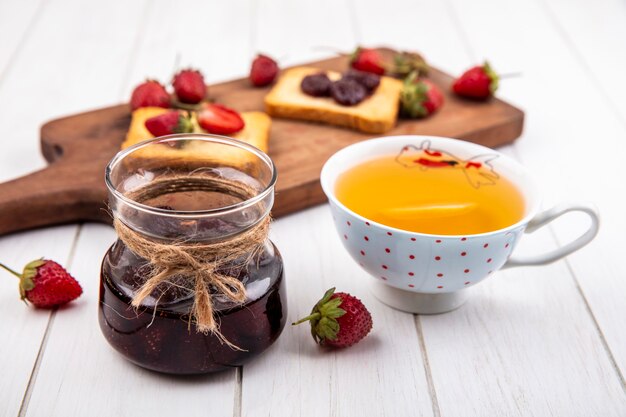 Vista dall'alto di marmellata di fragole con una tazza di tè con fragole fresche su un fondo di legno bianco