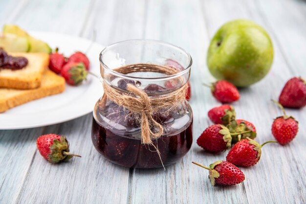 Vista dall'alto di marmellata di fragole su un barattolo di vetro con fragole fresche isolate su uno sfondo di legno grigio