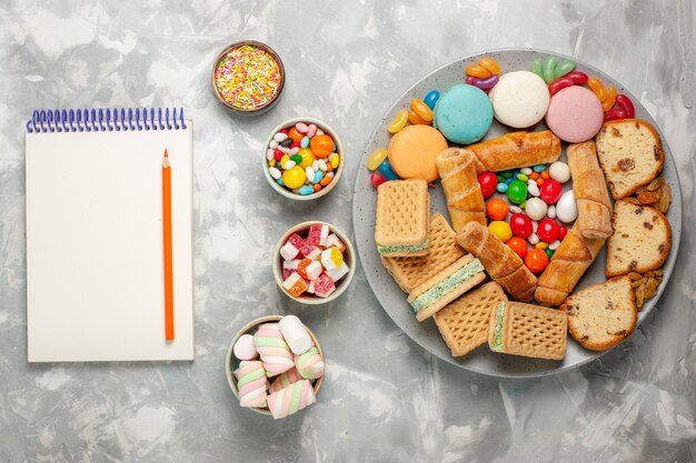 Vista dall'alto di marshmallow e caramelle con blocco note sulla superficie bianca