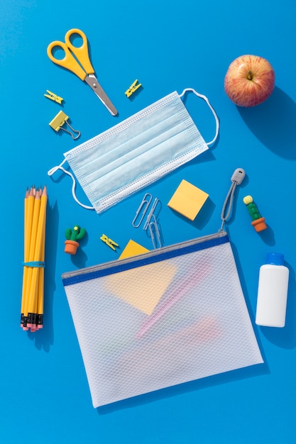 Vista dall'alto di materiale scolastico con maschera medica e mela