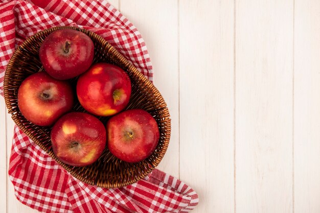 Vista dall'alto di mele rosse fresche su un secchio su un panno rosso controllato su una parete di legno bianca con spazio di copia