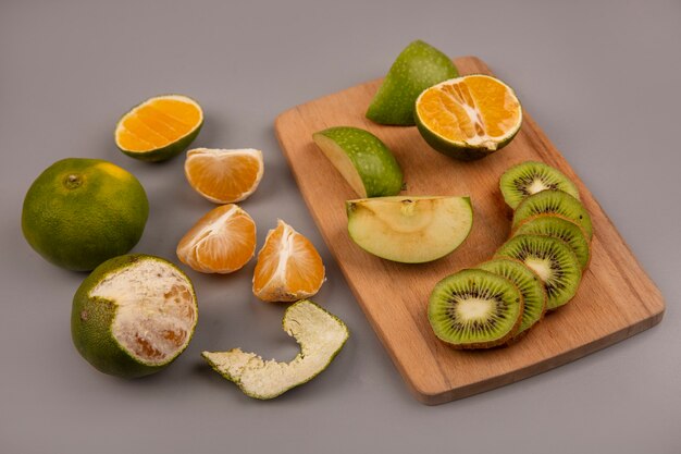 Vista dall'alto di mele verdi con fette di kiwi su una tavola di cucina in legno con mandarini isolati