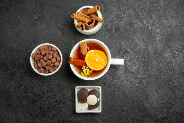 Vista dall'alto di nocciole al cioccolato ciotole di bastoncini di cannella cioccolato e nocciole e tazza di tè con cannella e limone sul lato sinistro del tavolo