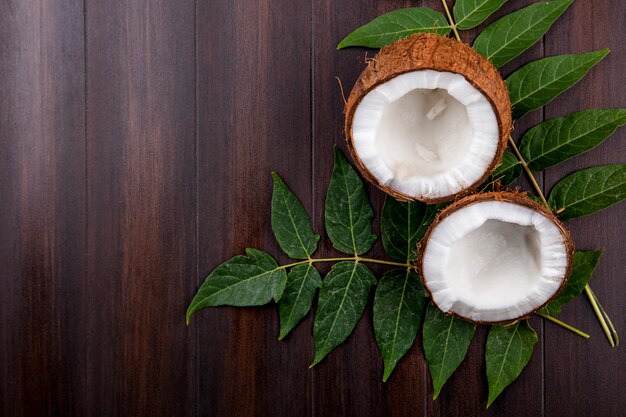 Vista dall'alto di noci di cocco fresche e marroni con foglie su legno