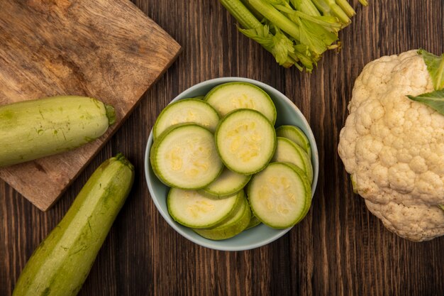 Vista dall'alto di organico di zucchine tritate su una ciotola con sedano zucchine e cavolfiore isolato su una superficie in legno