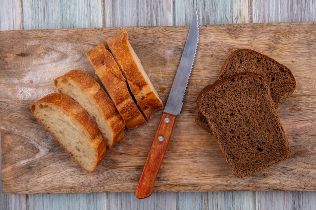 Vista dall'alto di pane come baguette a fette e quelli di segale con coltello sul tagliere su sfondo di legno