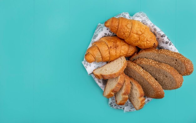 Vista dall'alto di pane come baguette di pannocchia con semi a fette e croissant nella ciotola su sfondo blu con spazio di copia