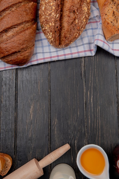 Vista dall'alto di pane come baguette vietnamite seminate e pane nero sul panno con burro mattarello latte su fondo in legno con spazio di copia