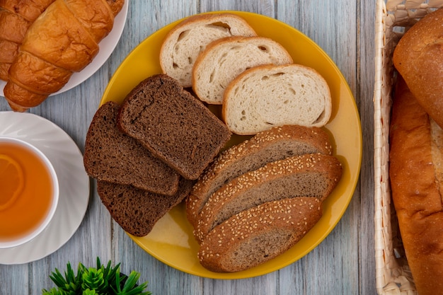 Vista dall'alto di pane come fette di pane marrone cob croissant baguette di segale e quelli bianchi in piastre e nel cestello con hot toddy su sfondo di legno