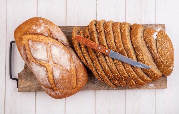 Vista dall'alto di pane come pannocchia con semi marrone a fette e pane croccante con coltello sul tagliere su sfondo di legno