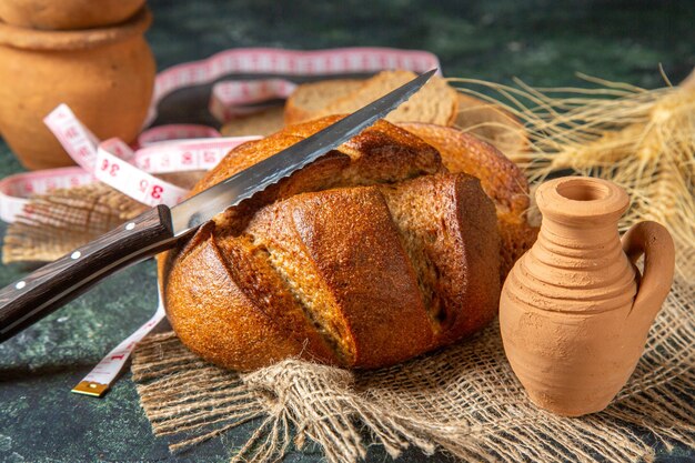 Vista dall'alto di pane nero intero e tagliato e punte su ceramiche di misuratore di asciugamano marrone su superficie di colori scuri