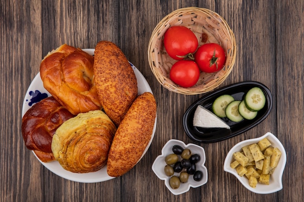Vista dall'alto di panini su un piatto con pomodori freschi su un secchio con olive su una ciotola su uno sfondo di legno