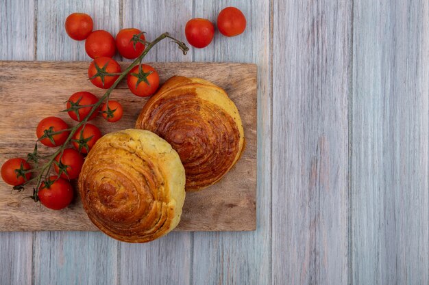 Vista dall'alto di panini su una tavola di cucina in legno con pomodori a grappolo freschi su uno sfondo di legno grigio con spazio di copia