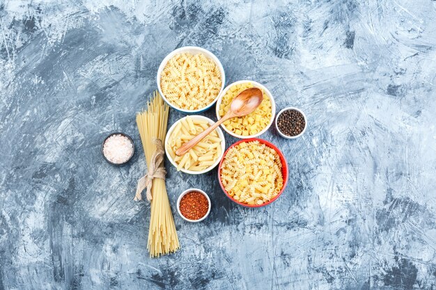 Vista dall'alto di pasta assortita in ciotole con spezie, cucchiaio di legno su sfondo grigio intonaco. orizzontale