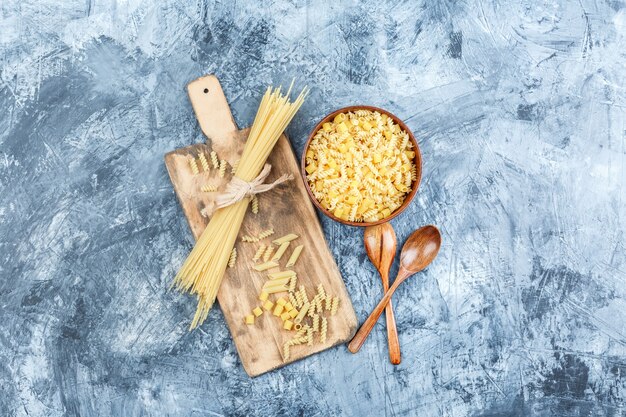 Vista dall'alto di pasta assortita in una ciotola con cucchiai di legno su intonaco grigio e sfondo tagliere. orizzontale