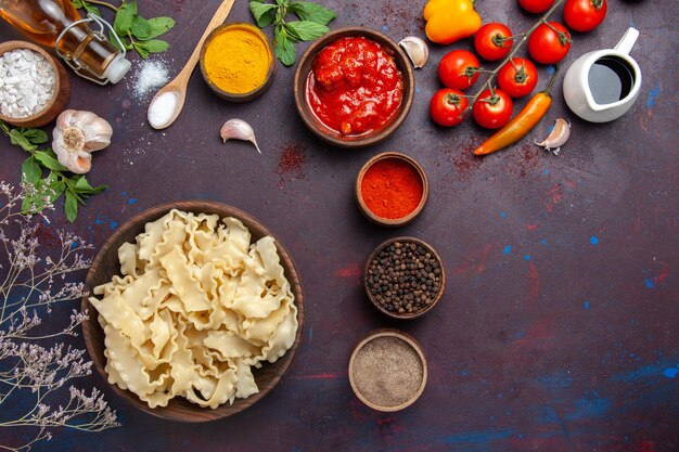 Vista dall'alto di pasta cruda a fette con pomodori rossi e condimenti diversi su sfondo scuro pasta pasta pasto cibo vegetale