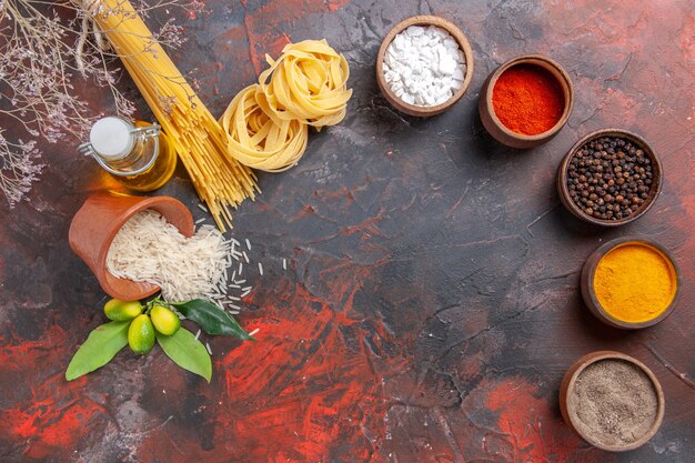 Vista dall'alto di pasta cruda con condimenti di olio e riso su una pasta di pasta cruda superficie scura