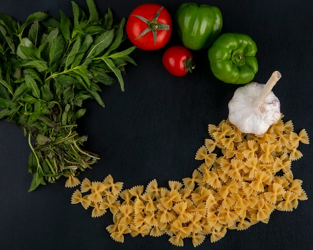 Vista dall'alto di pasta cruda con pomodori aglio e peperone con menta su una superficie nera