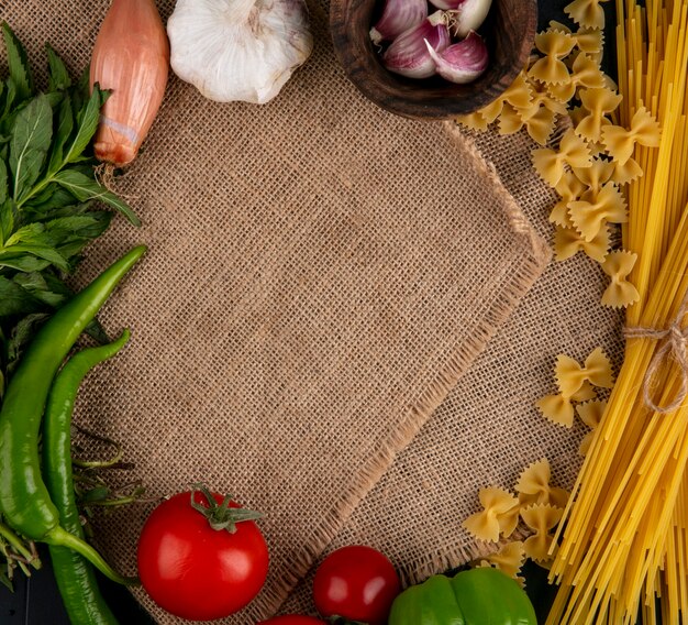 Vista dall'alto di pasta cruda con spaghetti crudi pomodori aglio cipolle e peperoncino su un tovagliolo beige