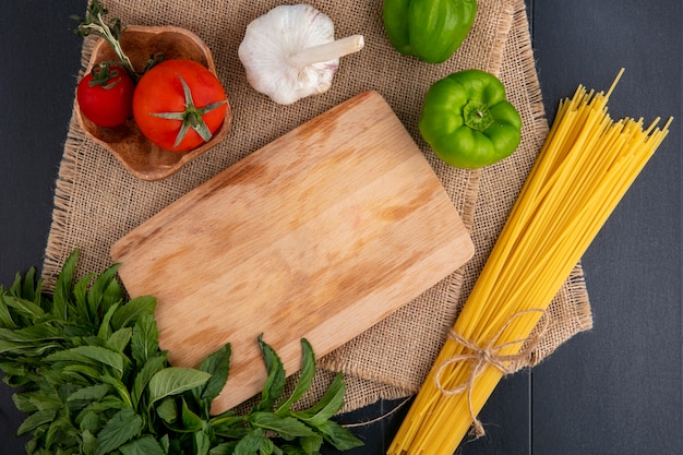 Vista dall'alto di pasta cruda con tagliere pomodori aglio menta e peperone su un tovagliolo beige