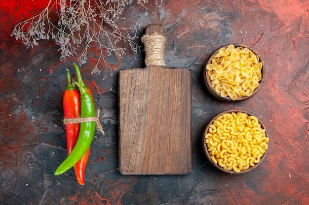 Vista dall'alto di pasta cruda peperoni di cayenna in diversi colori e dimensioni legati l'uno nell'altro con corda e tagliere di legno su sfondo di colore misto