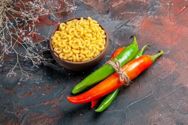 Vista dall'alto di pasta cruda peperoni di cayenna in diversi colori e dimensioni legati l'uno nell'altro con una corda su sfondo di colore misto