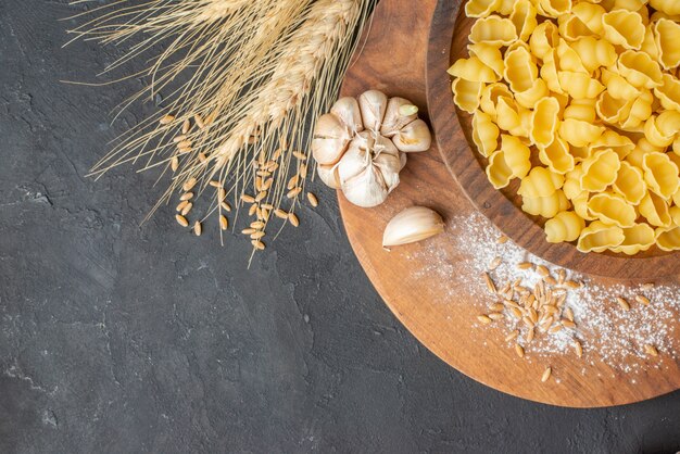 Vista dall'alto di pasta cruda su tagliere di legno garlics su tavola di colore scuro