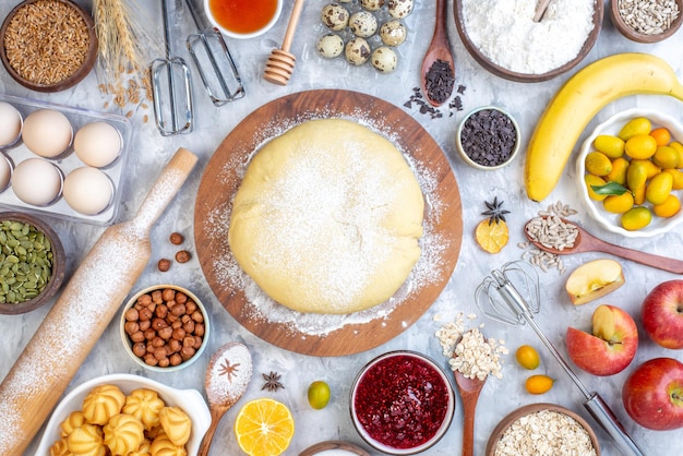 Vista dall'alto di pasta cruda su tavola di legno rotonda grattugia e set di cibi su sfondo di ghiaccio