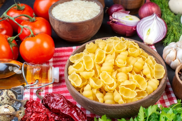 Vista dall'alto di pasta cruda su uova di riso rosse con asciugamano spogliate verdure fresche su tavola nera