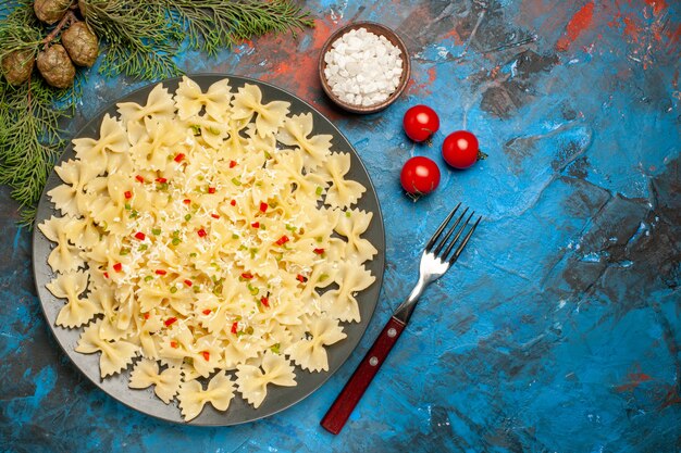 Vista dall'alto di pasta di farfalle con verdure pomodori sale e rami di abete forcella su sfondo blu