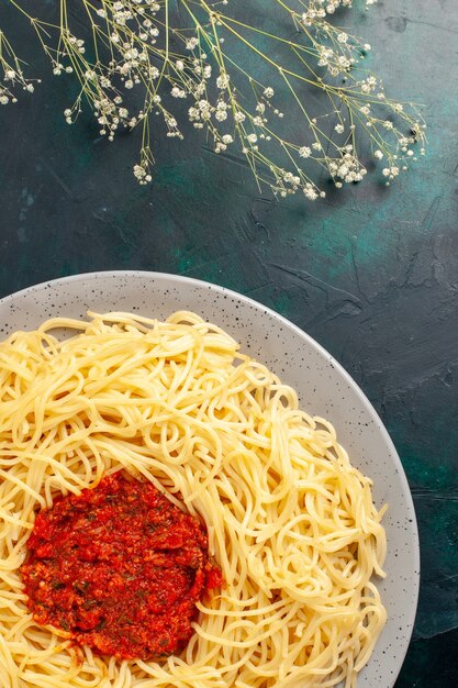 Vista dall'alto di pasta italiana cotta con carne di pomodoro tritata sulla superficie blu scuro