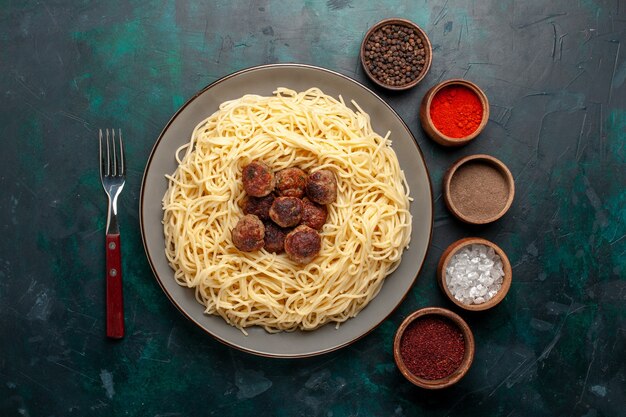 Vista dall'alto di pasta italiana cotta con polpette di carne e condimenti sulla superficie blu scuro