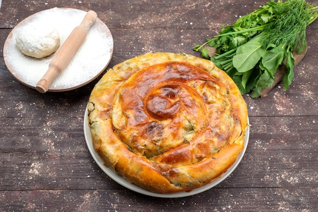 Vista dall'alto di pasticceria verde cotta rotonda all'interno del piatto bianco con verdure fresche sulla scrivania in legno marrone pasto cibo pasticceria pranzo verdi