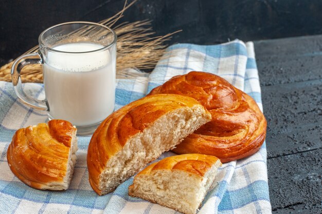 Vista dall'alto di pasticcini gustosi interi e tagliati su un asciugamano spogliato blu e latte a punta in un bicchiere su blu