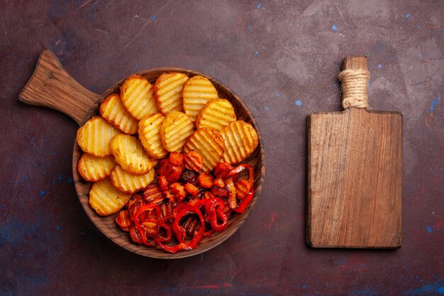 Vista dall'alto di patate al forno con verdure cotte all'interno del piatto nello spazio buio