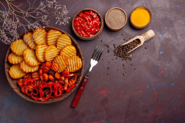 Vista dall'alto di patate al forno con verdure cotte e condimenti in uno spazio buio